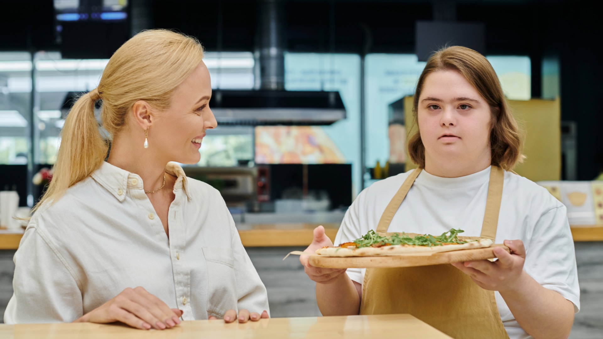 Young woman with disability at a pizza shop holding up a fire-grilled pizza